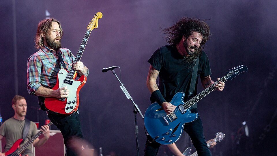 Dave Grohl performing on stage with Foo Fighters at Download Festival Paris in 2018, hair flying as he plays a blue electric guitar