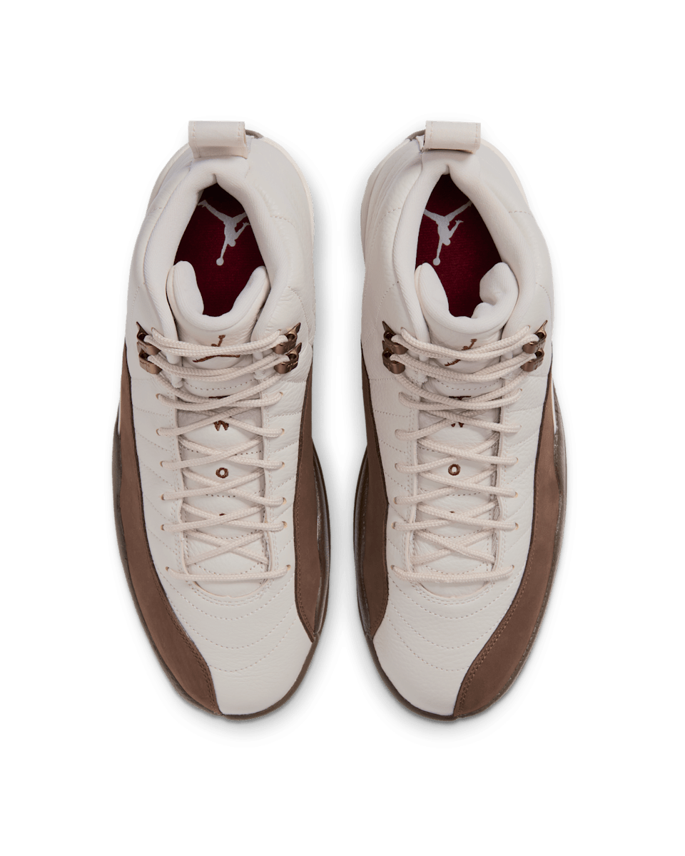 Nike's official product photograph of the Air Jordan 12 'Fireside' — the pair from above on a green studio background: cream orewood tumbled leather, cacao mudguards and team-red insoles with the white Jumpman