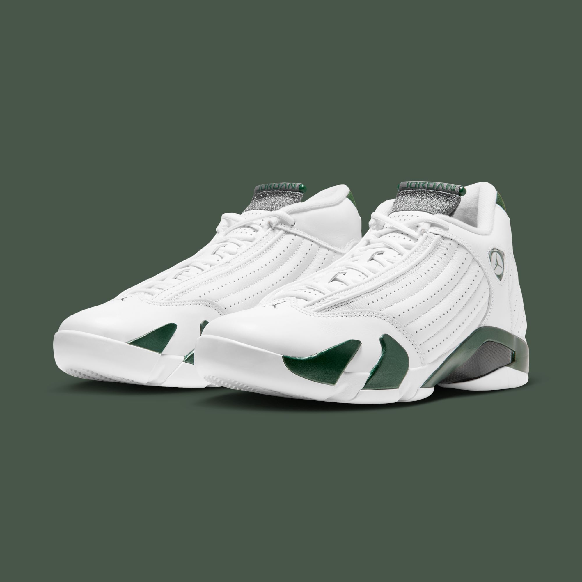 The Air Jordan 14 “Forest Green” pair in three-quarter view on Nike's solid gorge-green backdrop — white perforated leather uppers, deep green midsole teeth and heel wrap, graphite JORDAN tongues, the Jumpman shield badge at the ankle