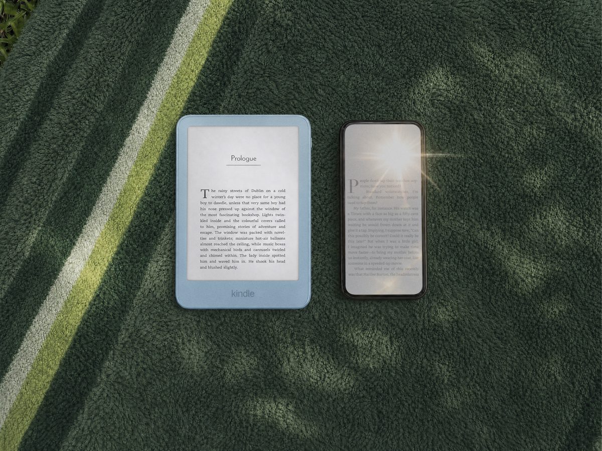 Two new 2026 Kindles with flush-front edge-to-edge displays resting on a striped beach towel — an Alpine Sky aluminum model and a Graphite model, both showing book text