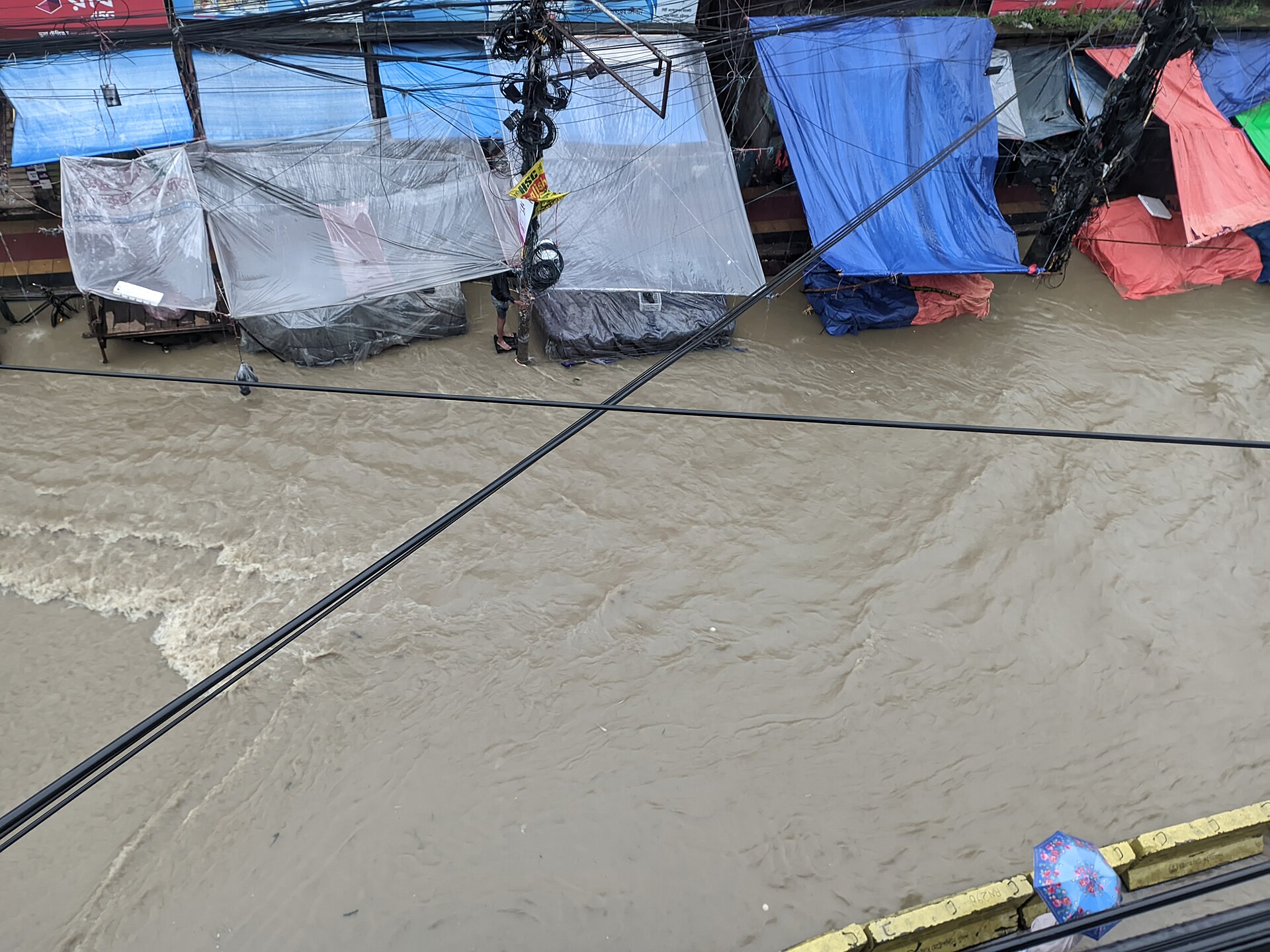 A flooded street in Bahaddarhat, Chittagong, with muddy floodwater surrounding makeshift tarp shelters (photographed during the 2024 floods).