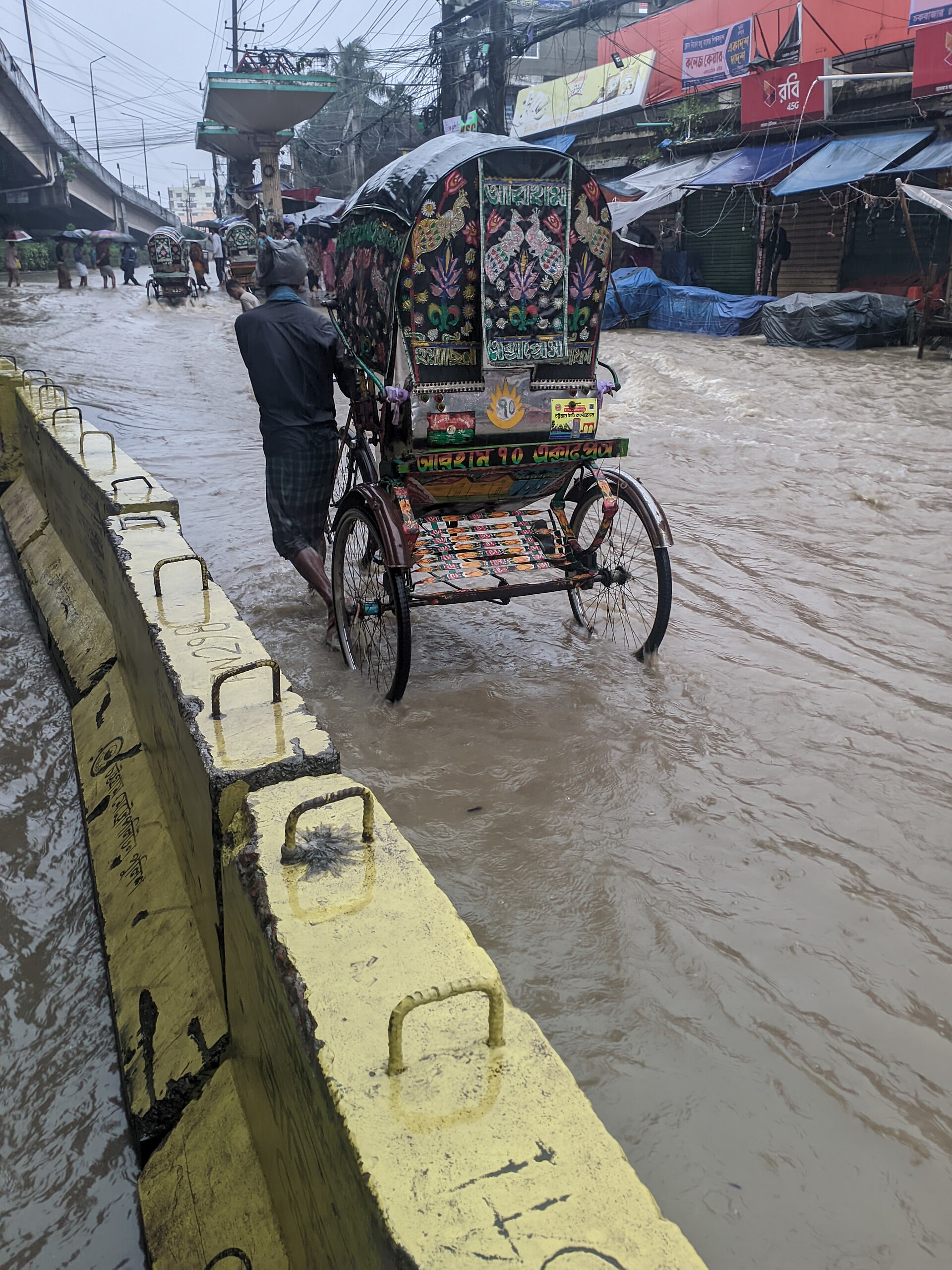 A rickshaw puller pushes his decorated rickshaw through a flooded street in Chittagong during the 2024 floods.