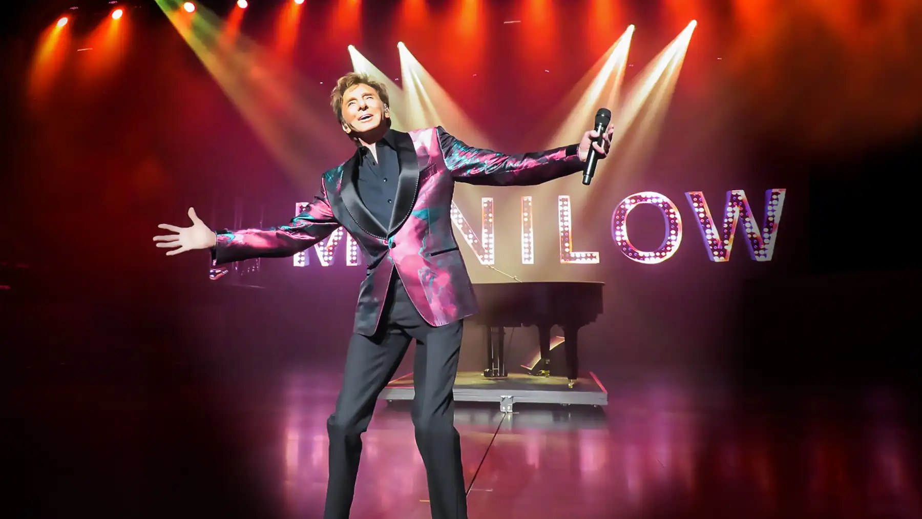 Barry Manilow performing on stage in front of giant illuminated MANILOW marquee letters
