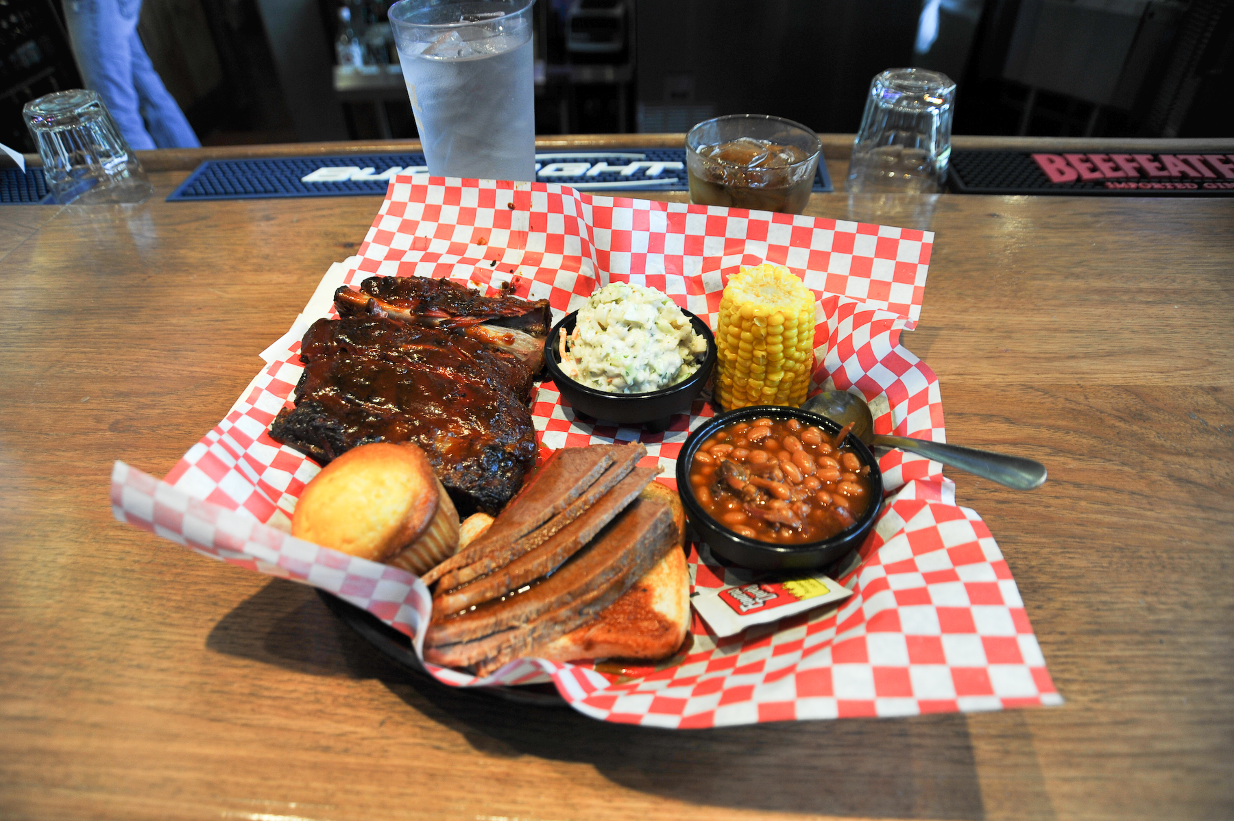 A Kansas City-style barbecue plate with ribs, brisket, corn, coleslaw, beans, and cornbread on a restaurant table