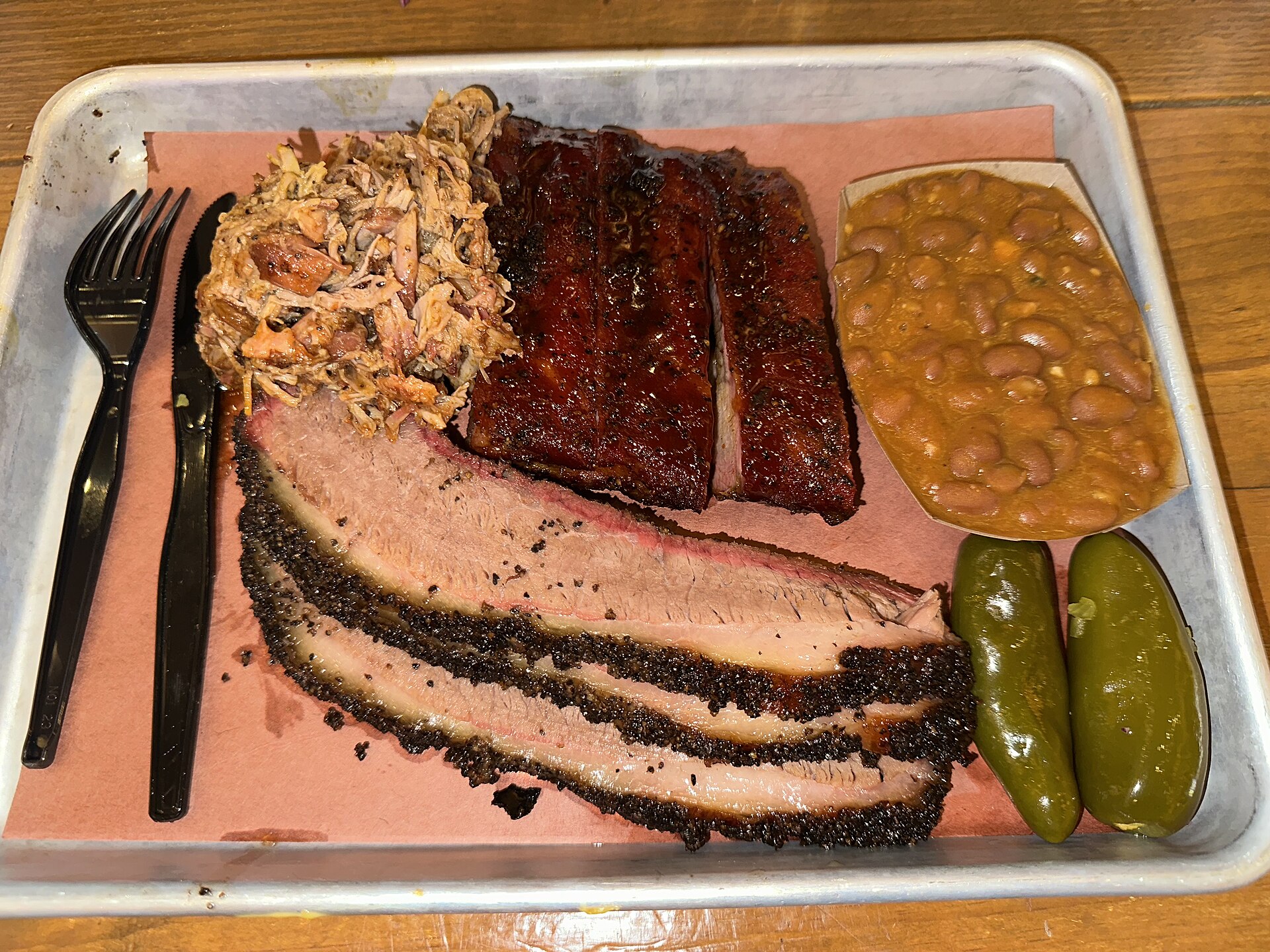 Sliced brisket, ribs, pulled pork, beans, and jalapeños on a tray at Pinkerton's BBQ in San Antonio