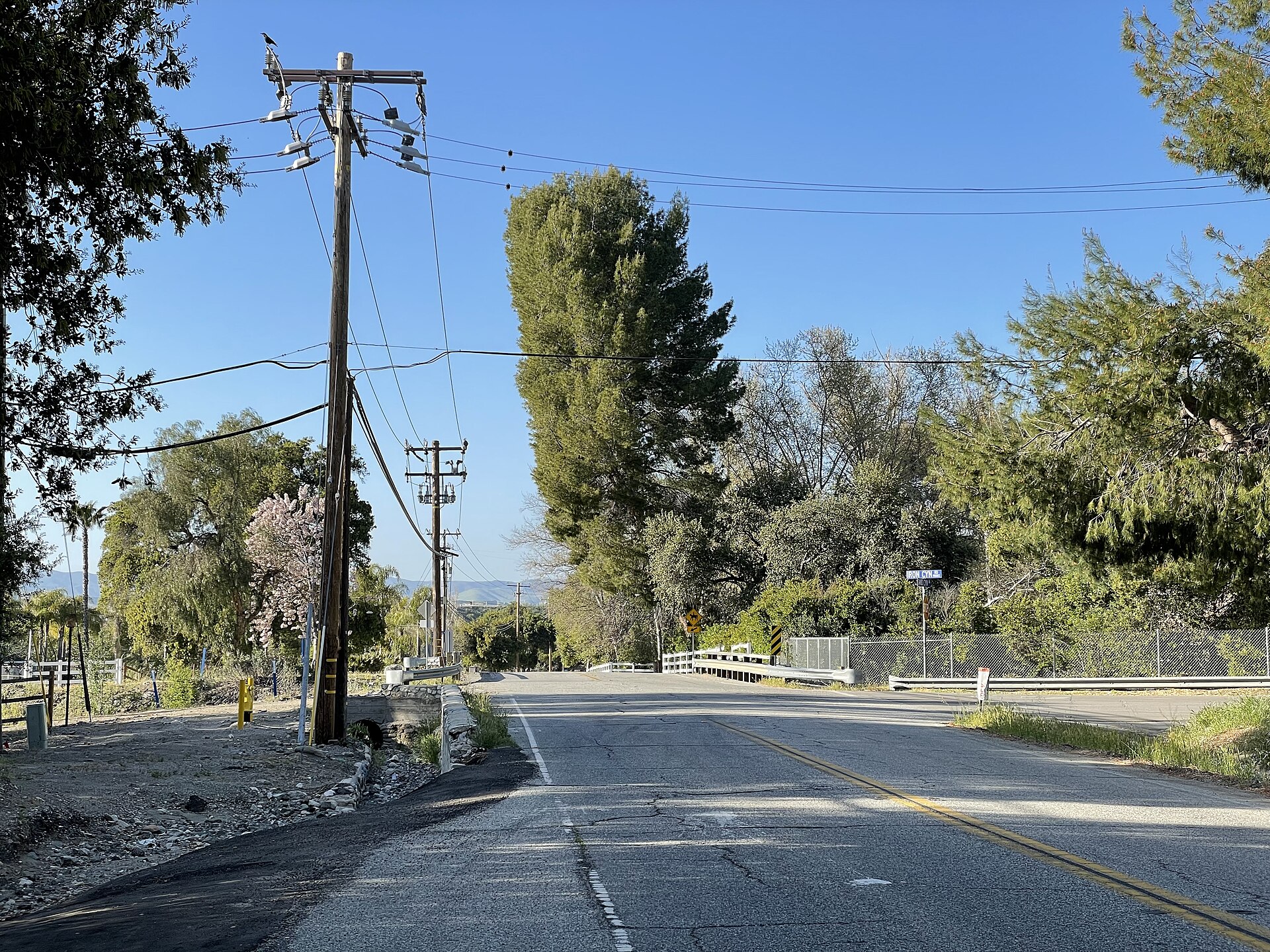 A quiet stretch of road in Sand Canyon, California on a clear sunny day, lined with trees and power poles