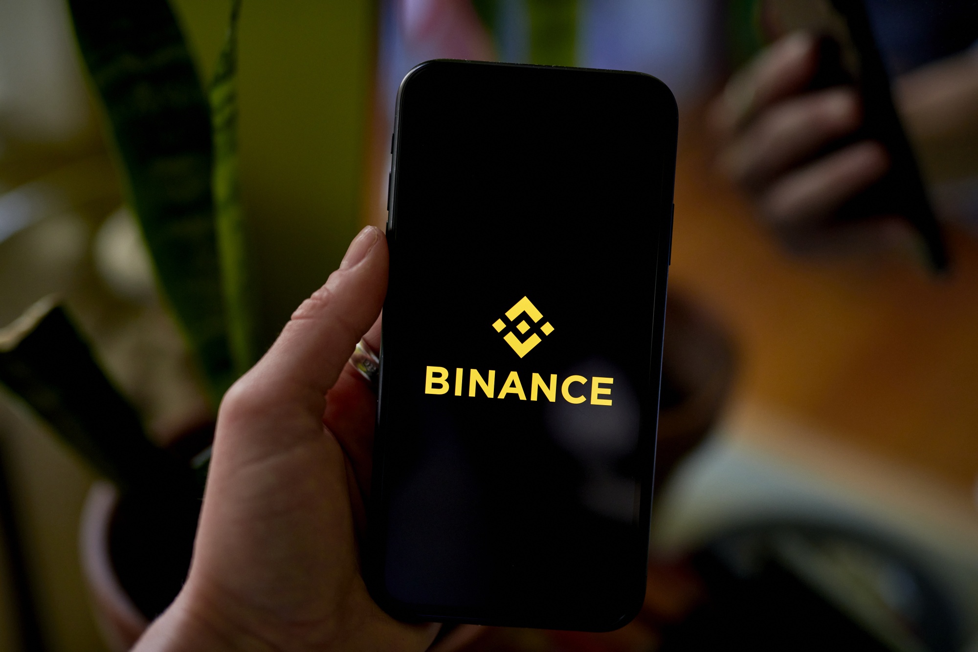 A hand holds a smartphone showing the Binance app logo.