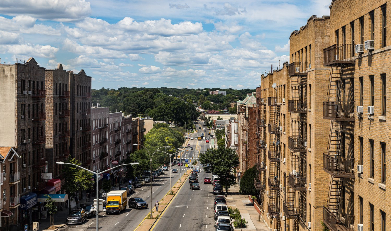 Brick apartment buildings line a Bronx street under a bright blue sky
