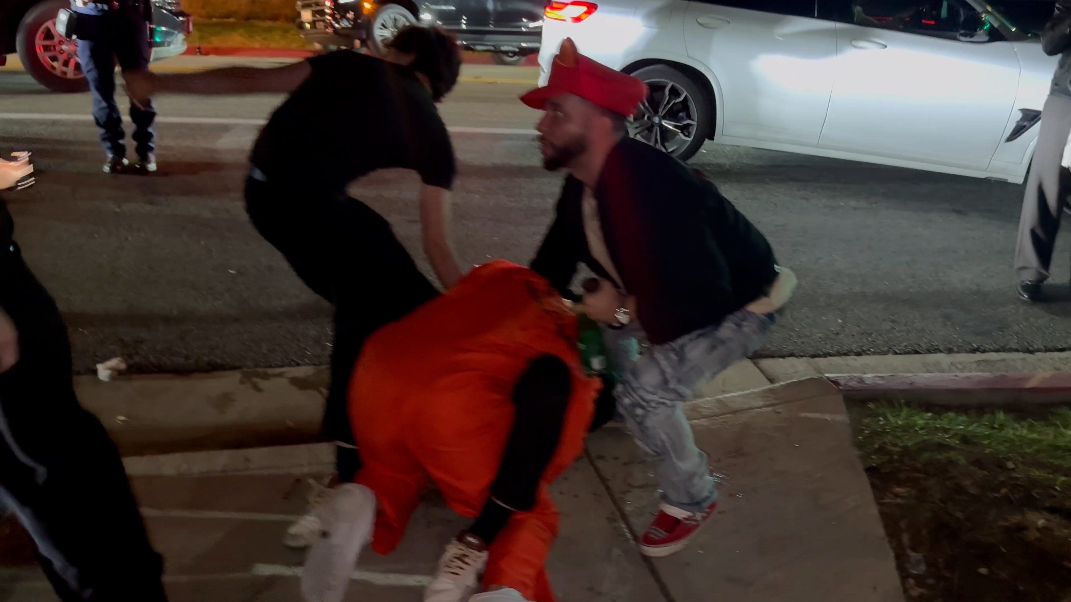 A frame from the brawl video: Bryce Hall in the orange inmate jumpsuit on the sidewalk, pulled down by two men as the fight is broken up outside the party.