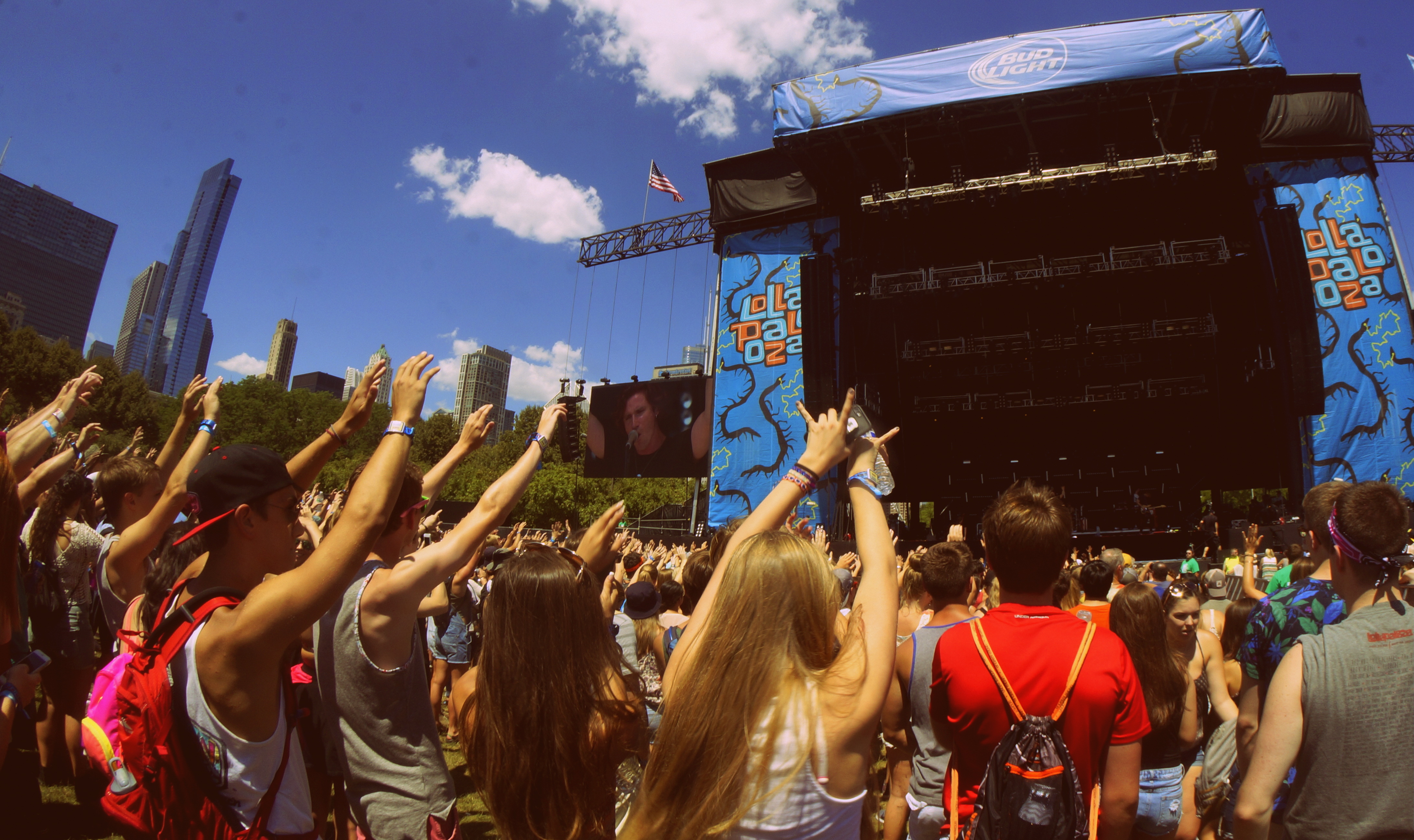 A daylight festival crowd with hands raised in front of a main stage at Lollapalooza Chicago