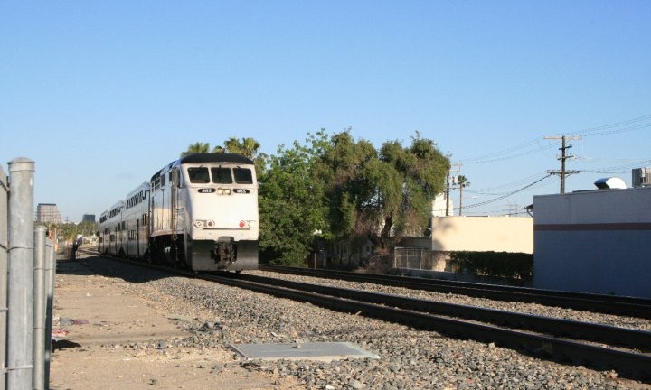 A Metrolink commuter train approaching on tracks under a clear blue sky
