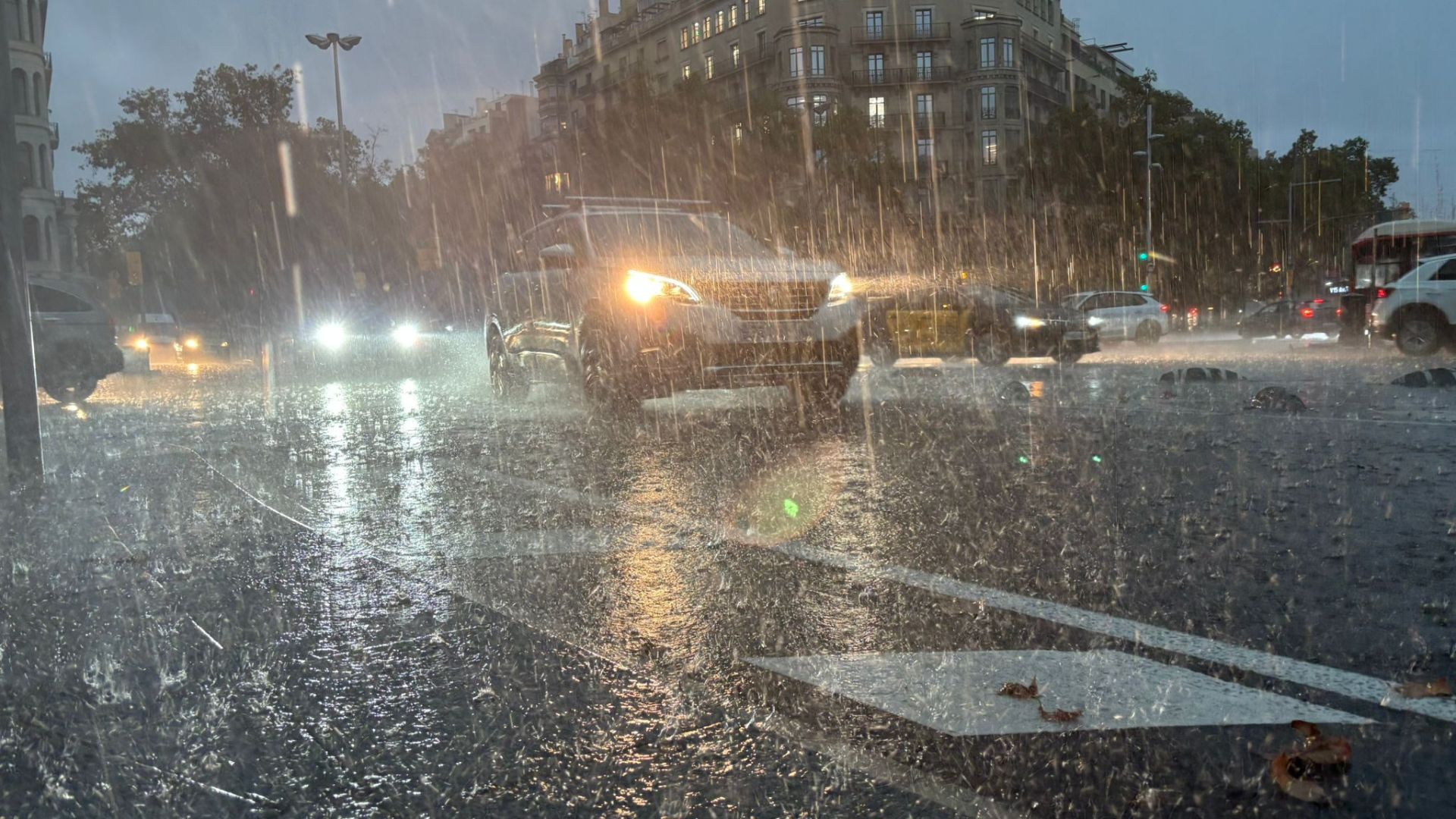 Rain lashes a Barcelona street as cars with headlights on push through standing water during severe storm flooding in Catalonia