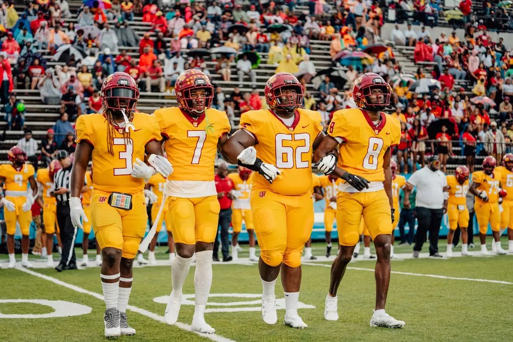 Tuskegee Golden Tigers players in gold uniforms walk onto the field