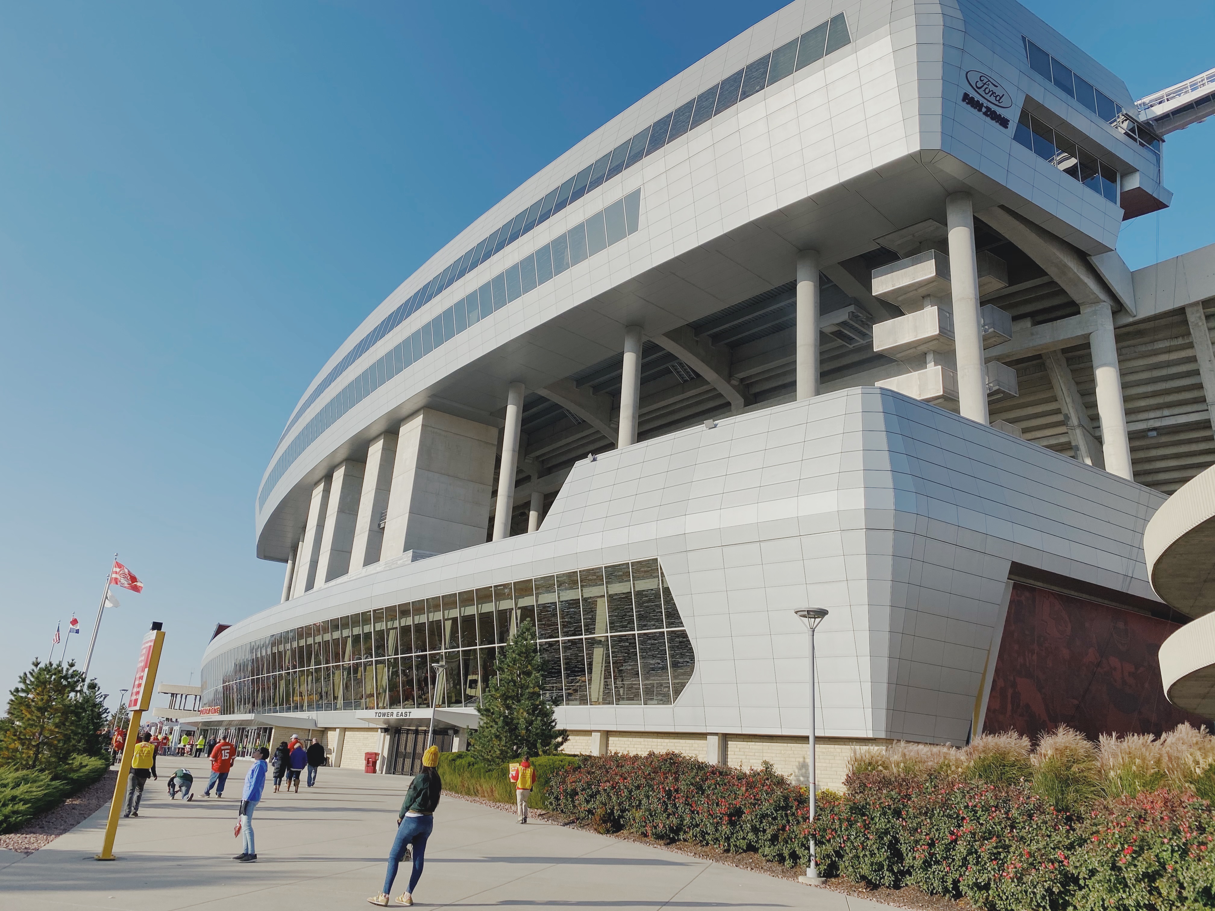 Fans walking toward the Tower East entrance of Arrowhead Stadium under a clear blue sky on game day.