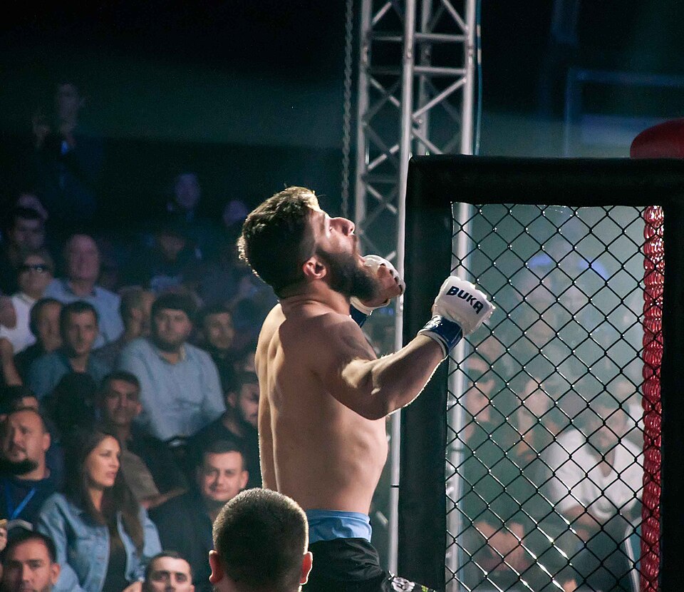 An MMA fighter celebrates a win inside the cage in front of a roaring crowd