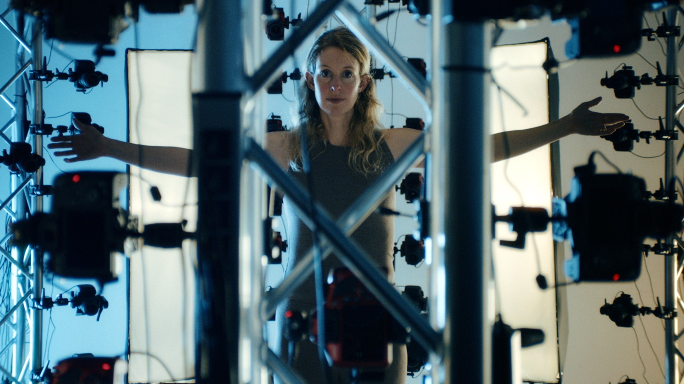 A still from 'You Can See Everything': Elizabeth Holmes standing inside an array of cameras pointed at her from every side