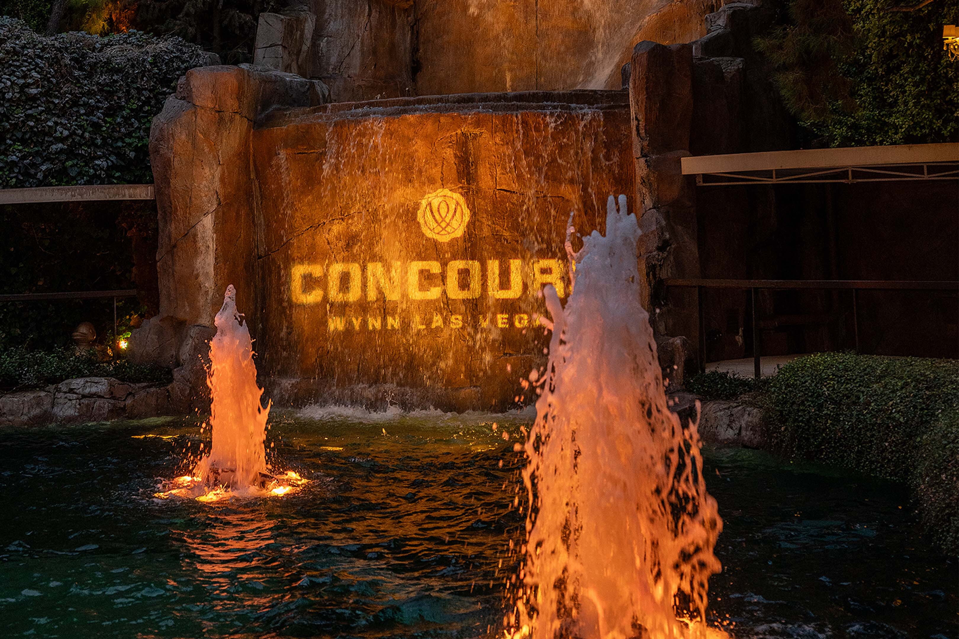 The Concours at Wynn mark projected in gold onto the Wynn waterfall at night, fountains lit below — event file photography from a prior edition