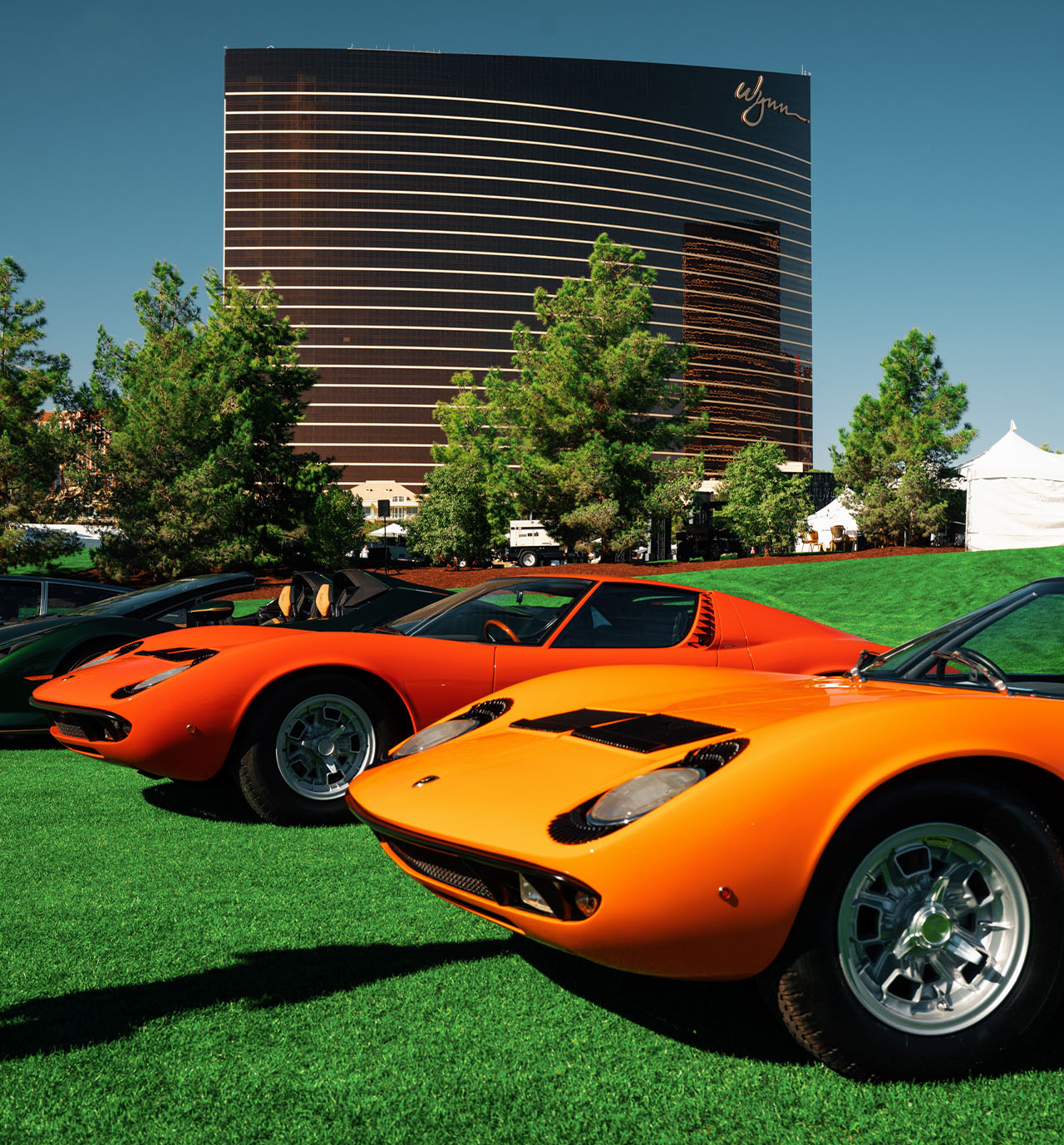 Two orange Lamborghini Miuras on the grass below the Wynn tower — event file photography from a prior edition