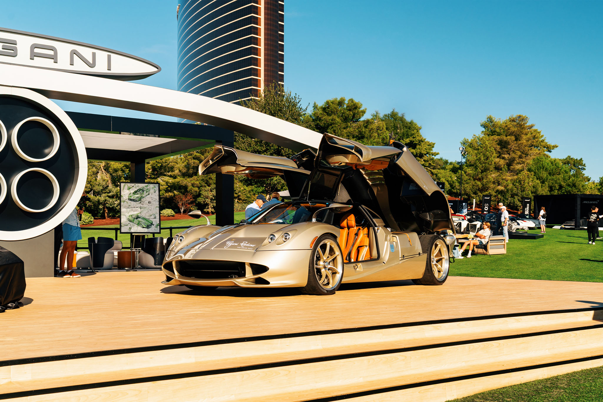 A gold Pagani Huayra Codalunga with its doors raised on the Pagani stand at a prior Concours at Wynn, the Wynn tower behind — event file photography