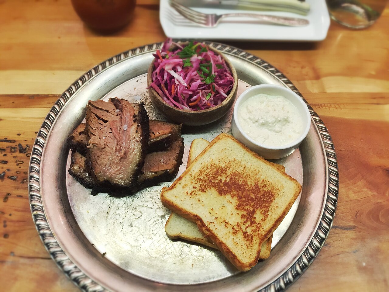 A plate of slow-smoked barbecue with ribs, brisket and sides in bright daylight