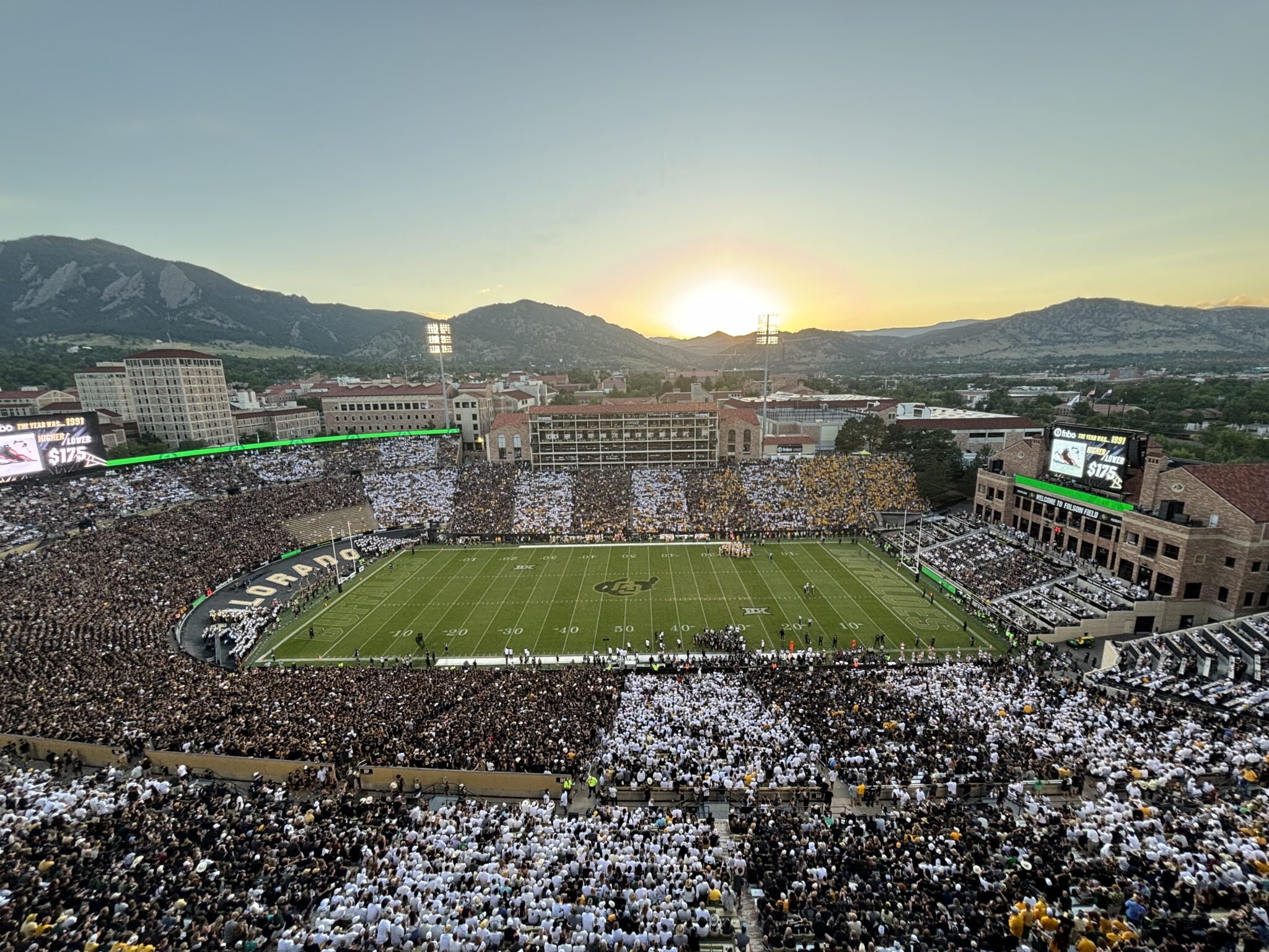 Folsom Field at sunset with a packed crowd and the Boulder Flatirons beyond