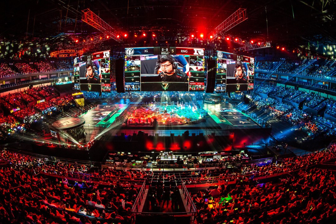 A packed Chinese esports arena under red lights during an international League of Legends match.