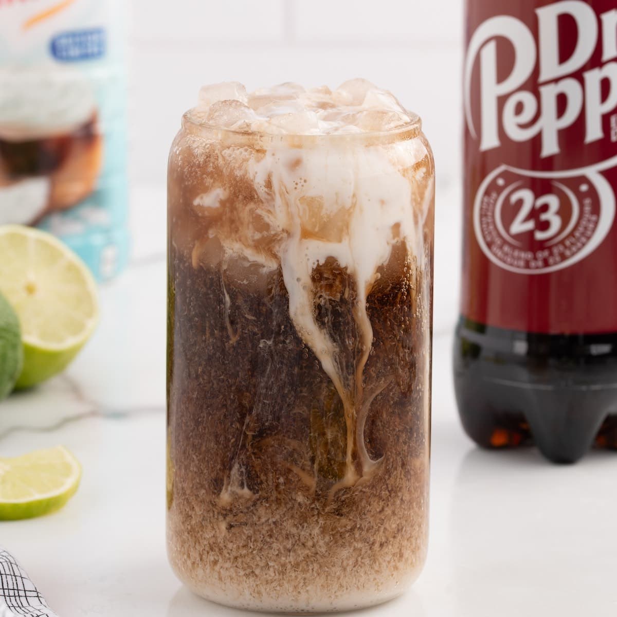 A dirty Dr Pepper with cream swirling through the ice in a bright glass