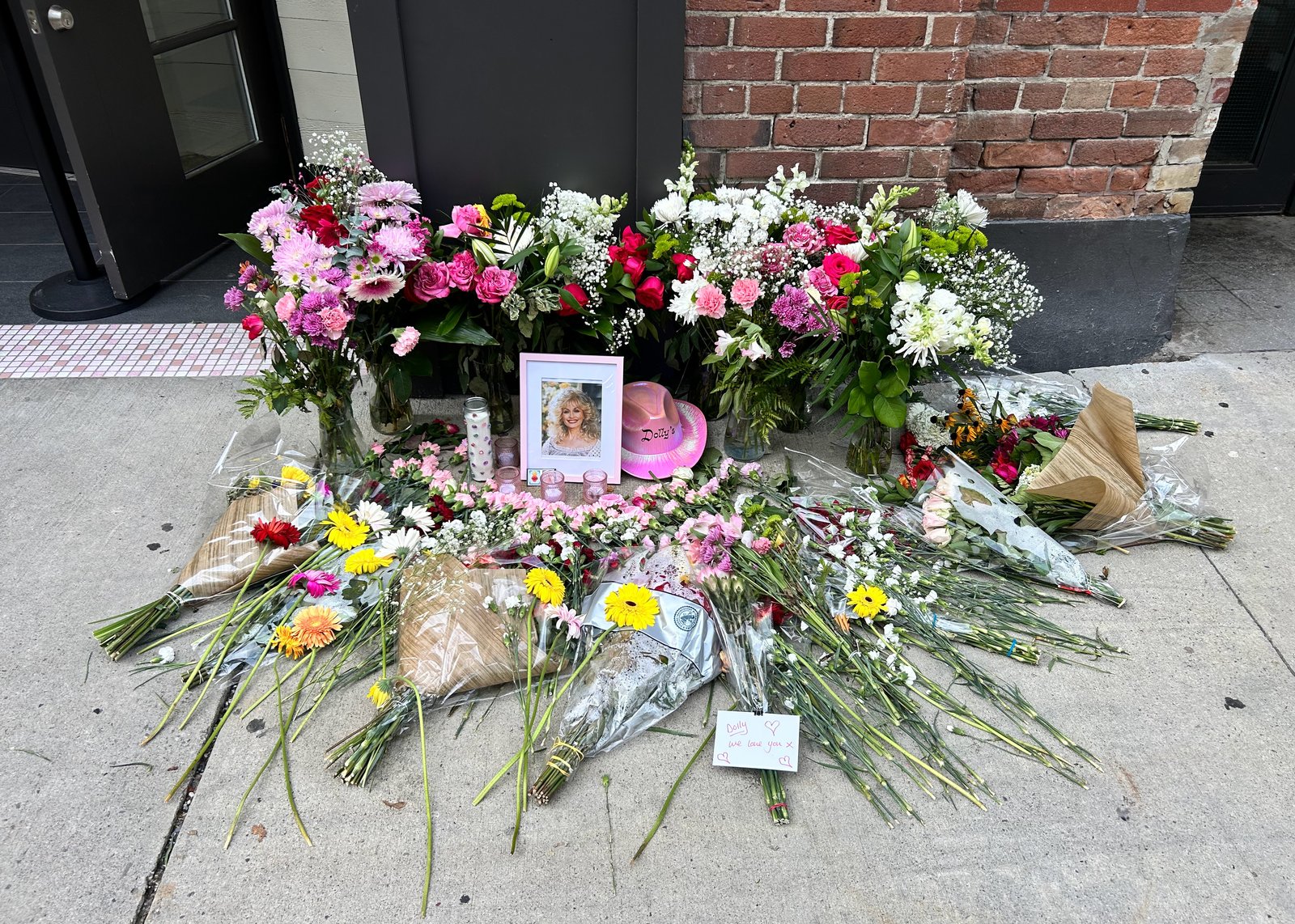 Flowers, candles, and handwritten notes left at a memorial for Dolly Parton outside Dolly's bar in Toronto