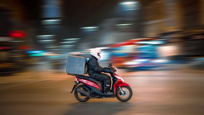 A delivery courier on a scooter at night