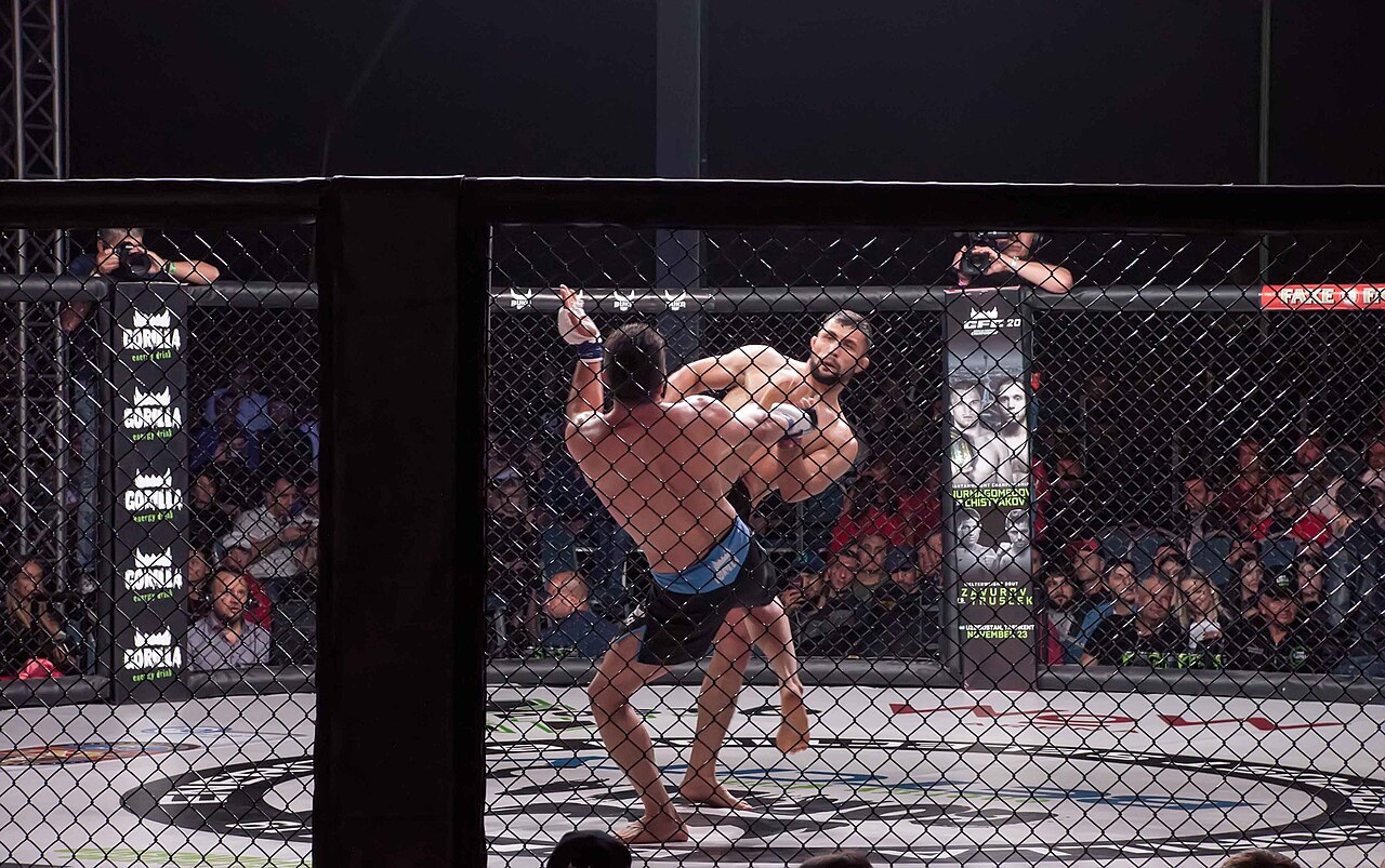 Two MMA fighters exchanging in a caged arena in front of a crowd
