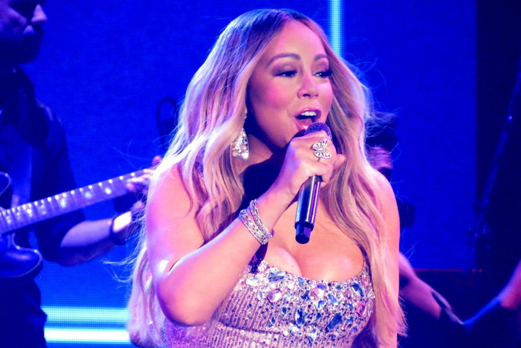 Mariah Carey performing on her Caution World Tour, singing into a microphone under blue stage lights