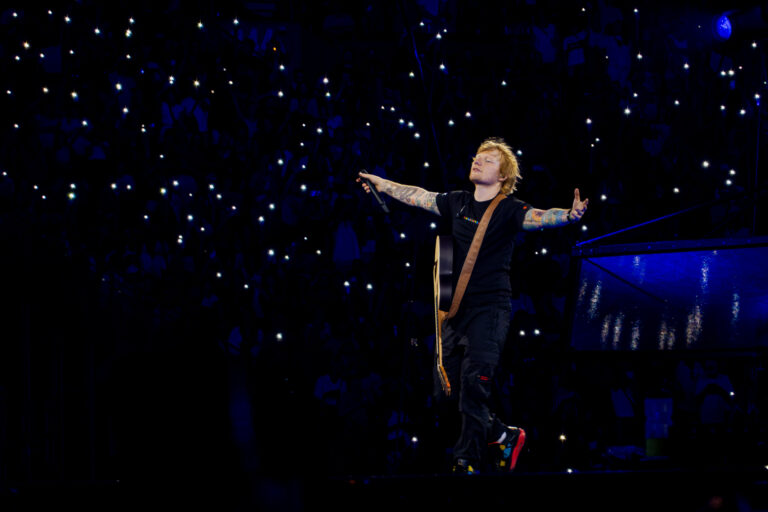 Ed Sheeran performing live on stage in front of a large crowd.