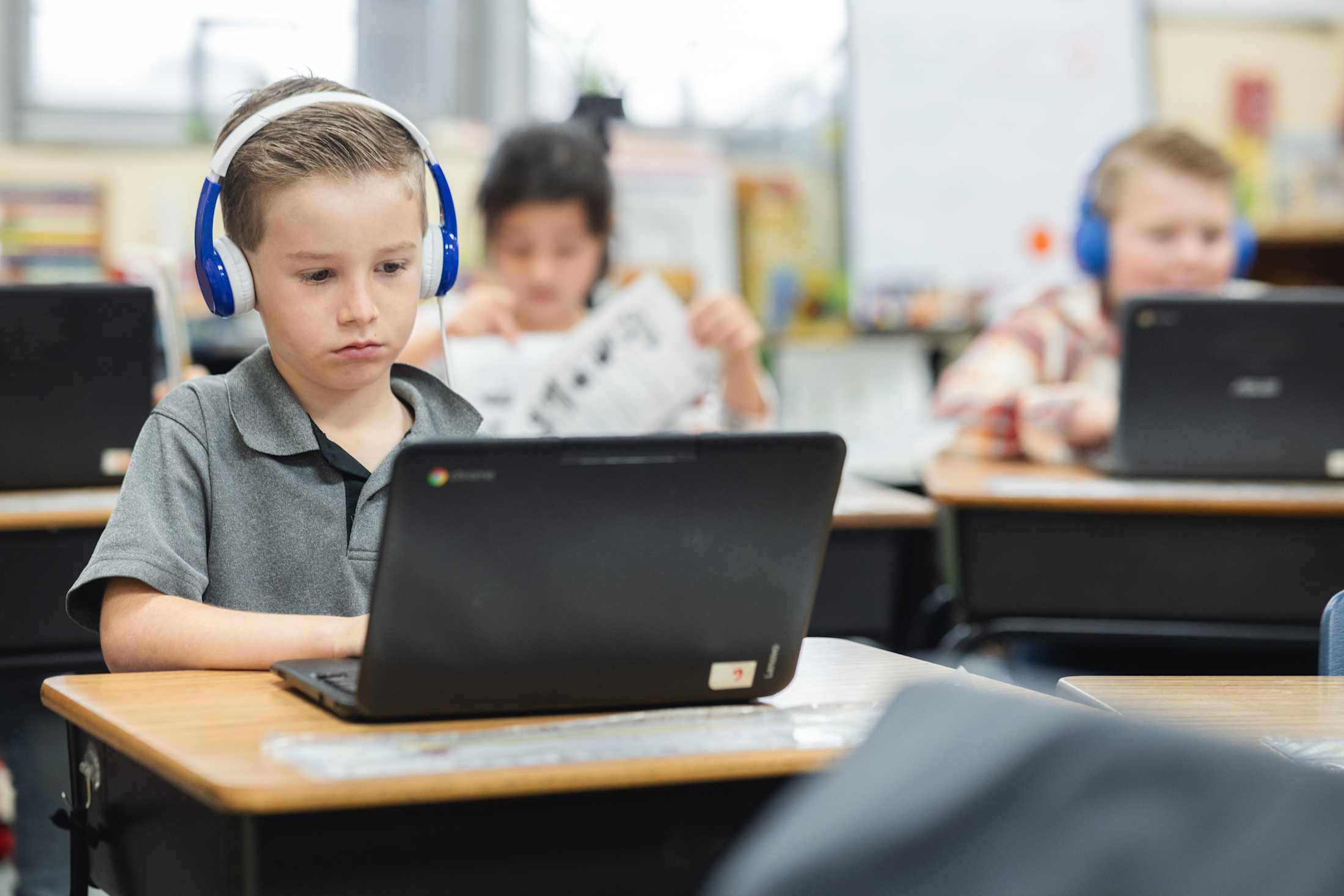 An elementary student wearing headphones works on a Chromebook in a classroom