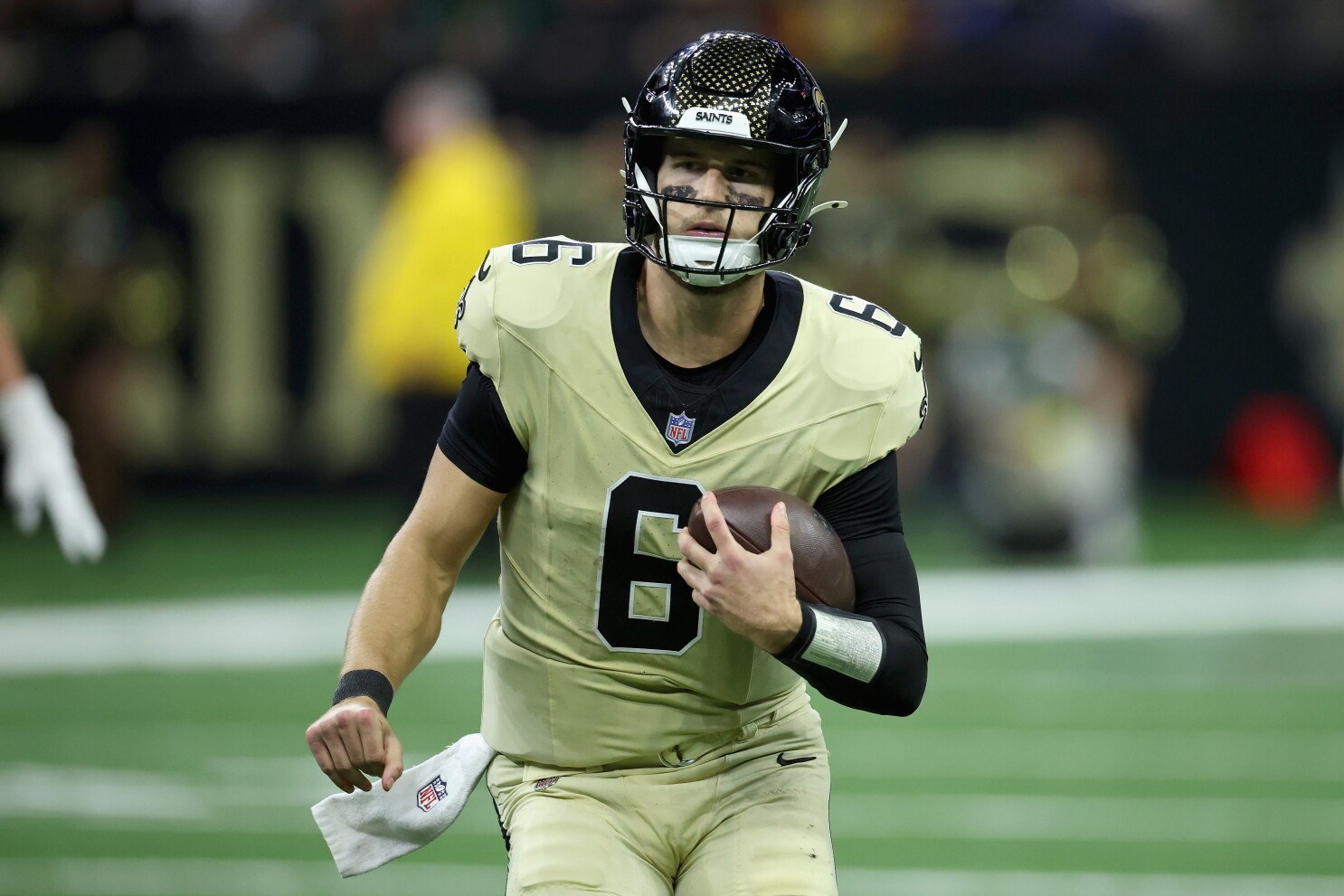 New Orleans Saints quarterback Tyler Shough in the gold home uniform holding the football.