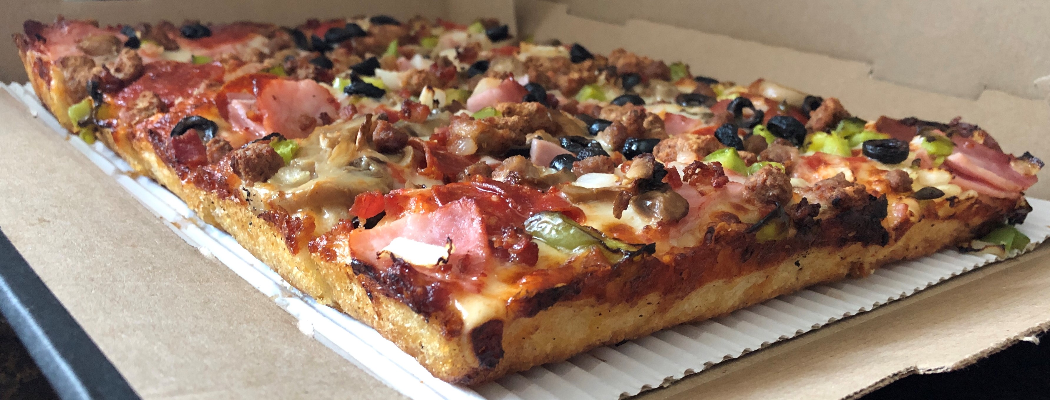 A Detroit-style square pizza with a thick caramelized cheese crust in a pan