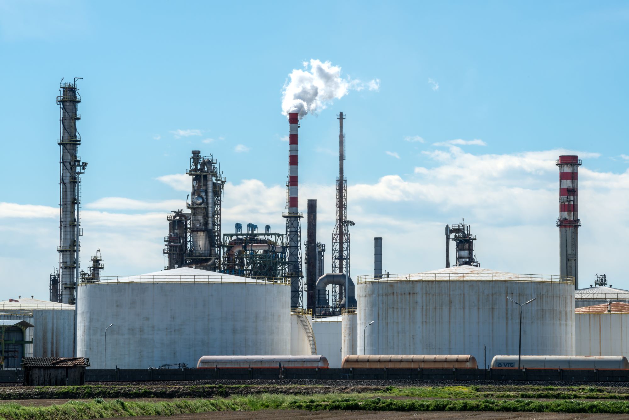 An oil refinery with crude-oil storage tanks under a bright blue sky