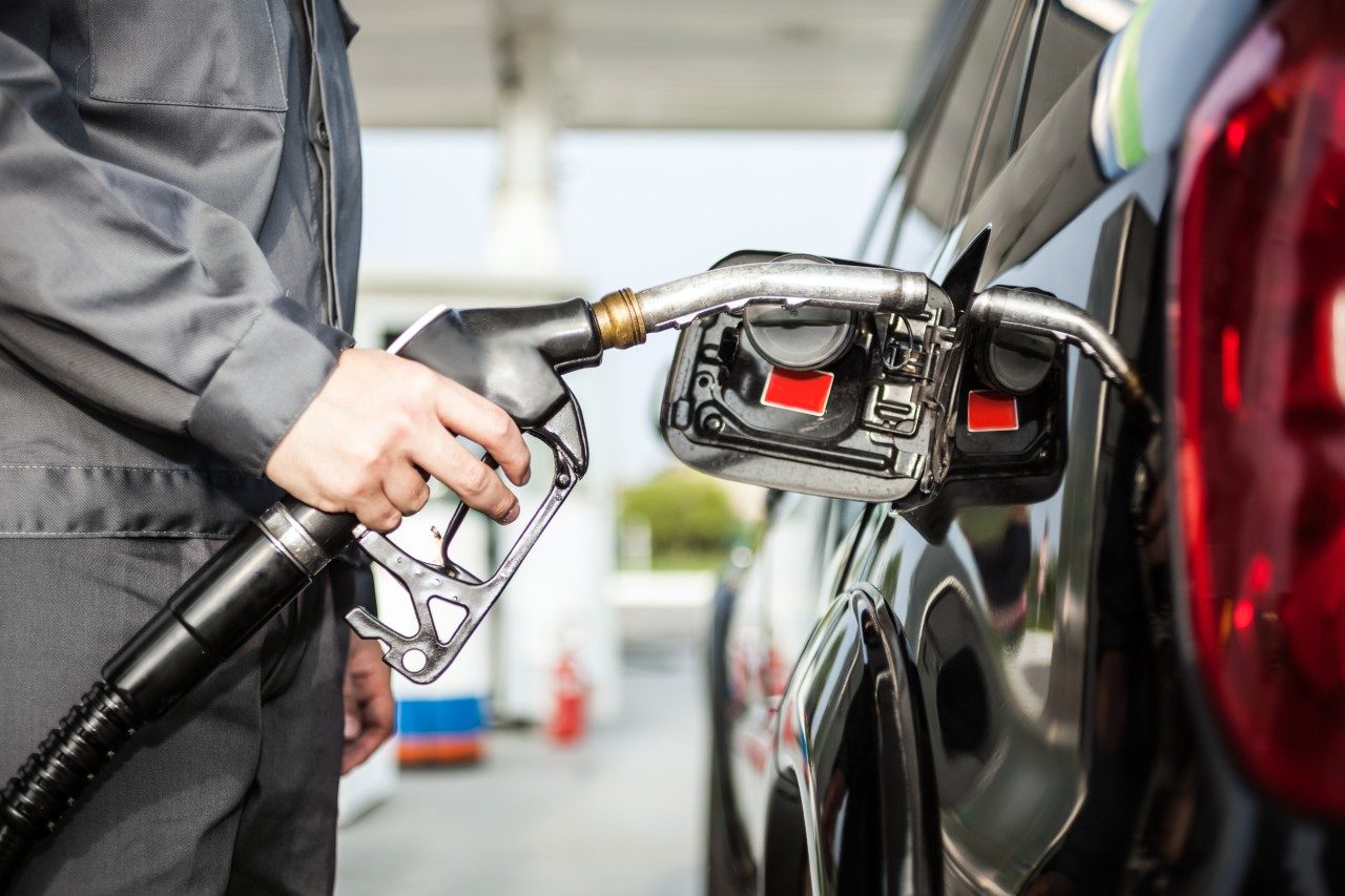A driver refueling a car at a gas station pump in daylight