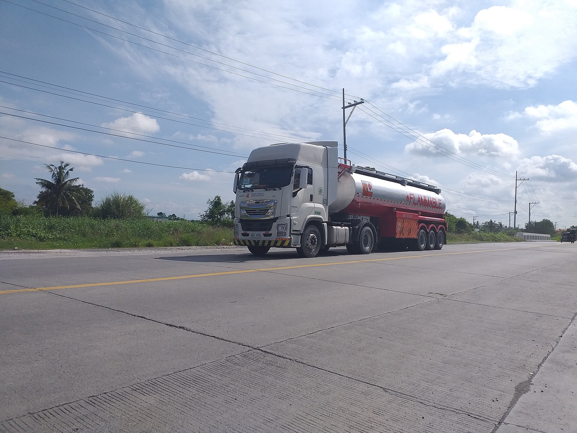 A white fuel tanker truck with a red flammable-materials trailer on a highway under a bright blue sky