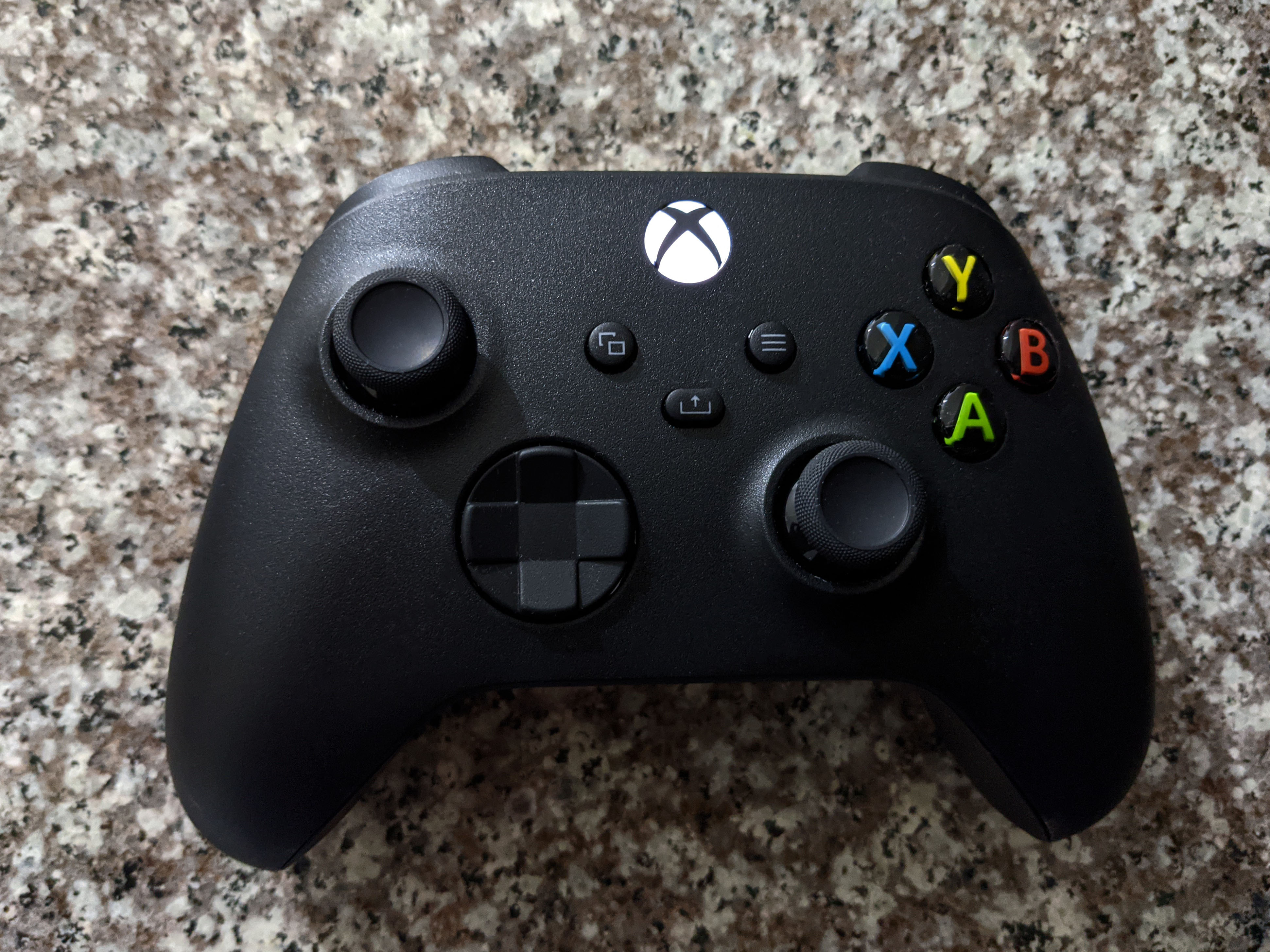 A black Xbox wireless controller with its colorful ABXY buttons, photographed on a stone surface
