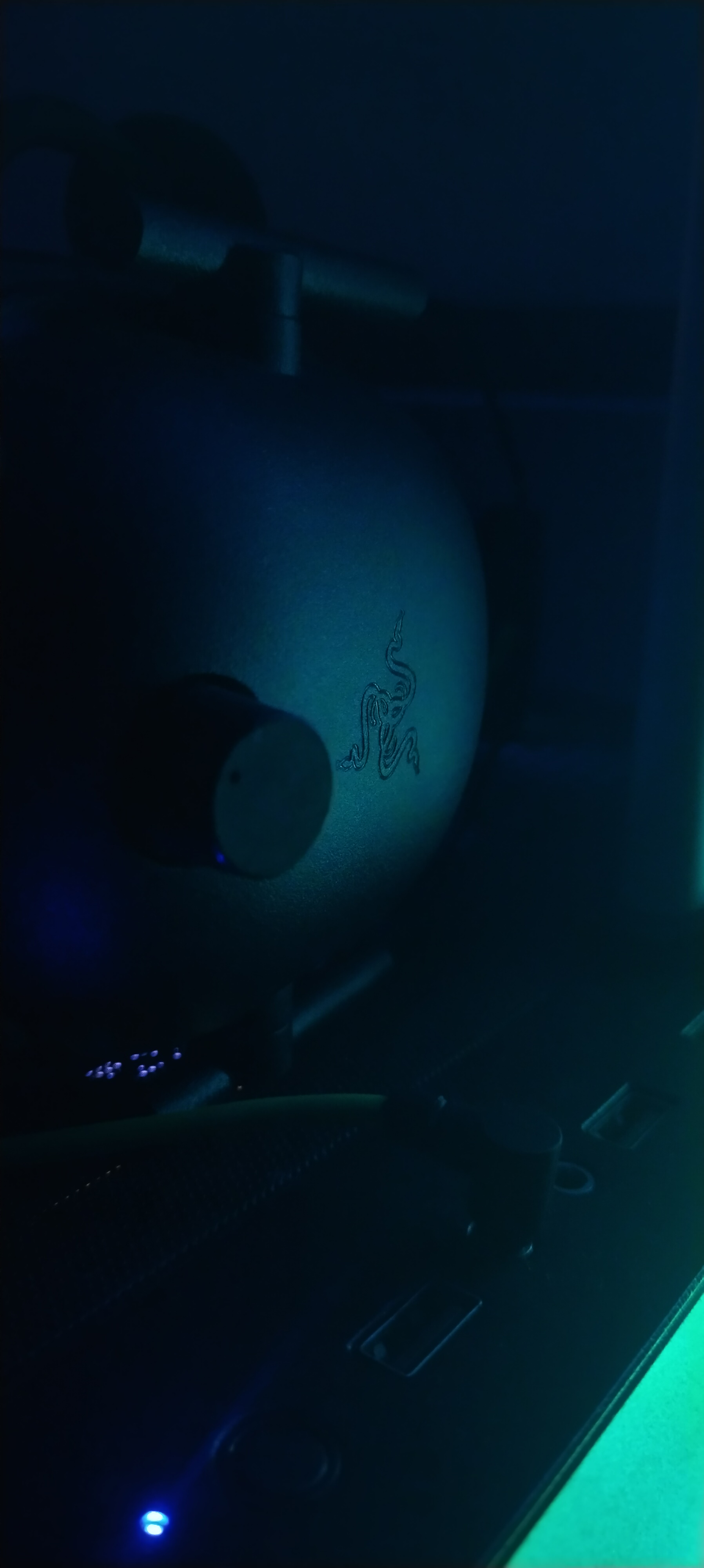 A gaming headset glowing under teal RGB lighting on a desk, next to a backlit keyboard