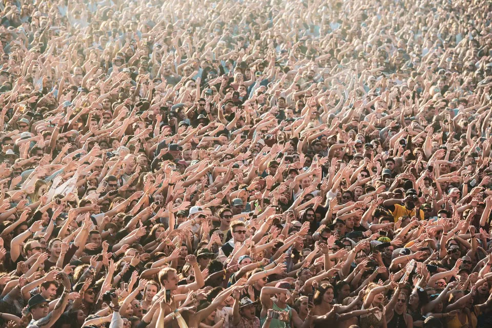 A daytime festival crowd with hands in the air — Grimes announced her new album PSYOPERA on Friday