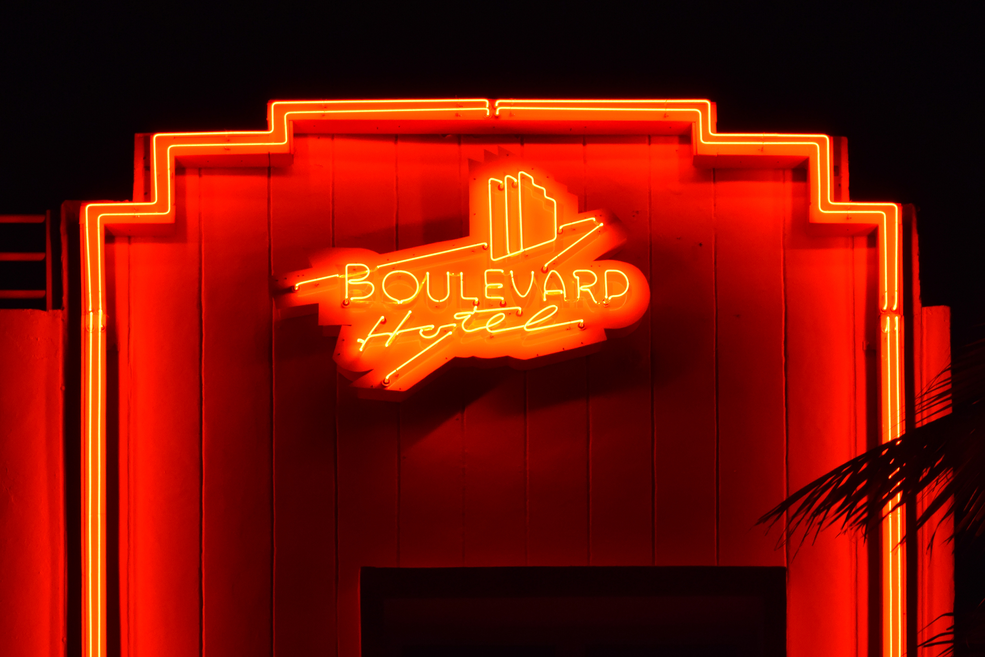 The red neon sign of the Boulevard Hotel glowing on Miami Beach at night, with palm fronds in the frame