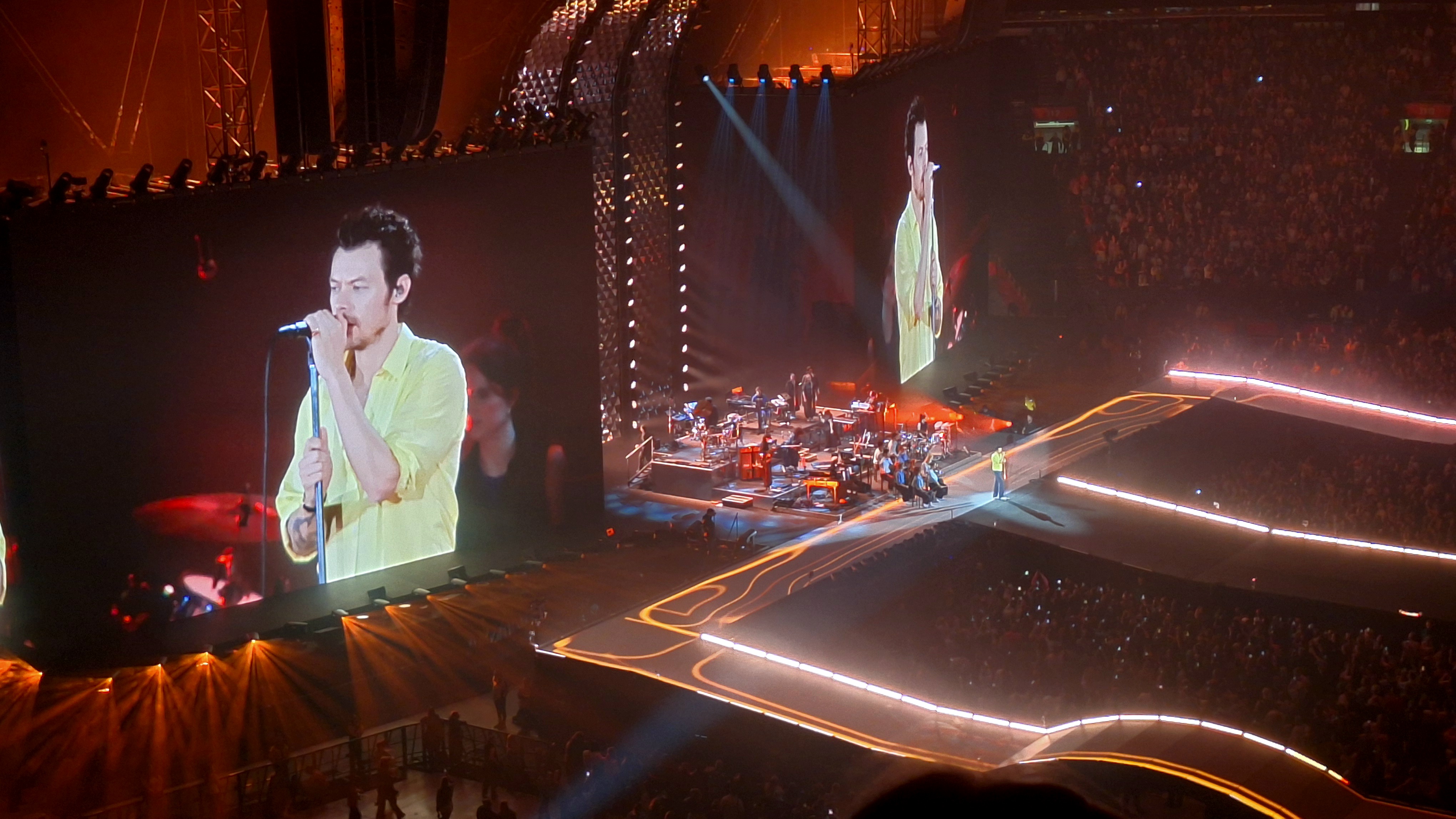 Harry Styles performing on the Together, Together tour — arena wide shot with Styles on the stage screens and runway