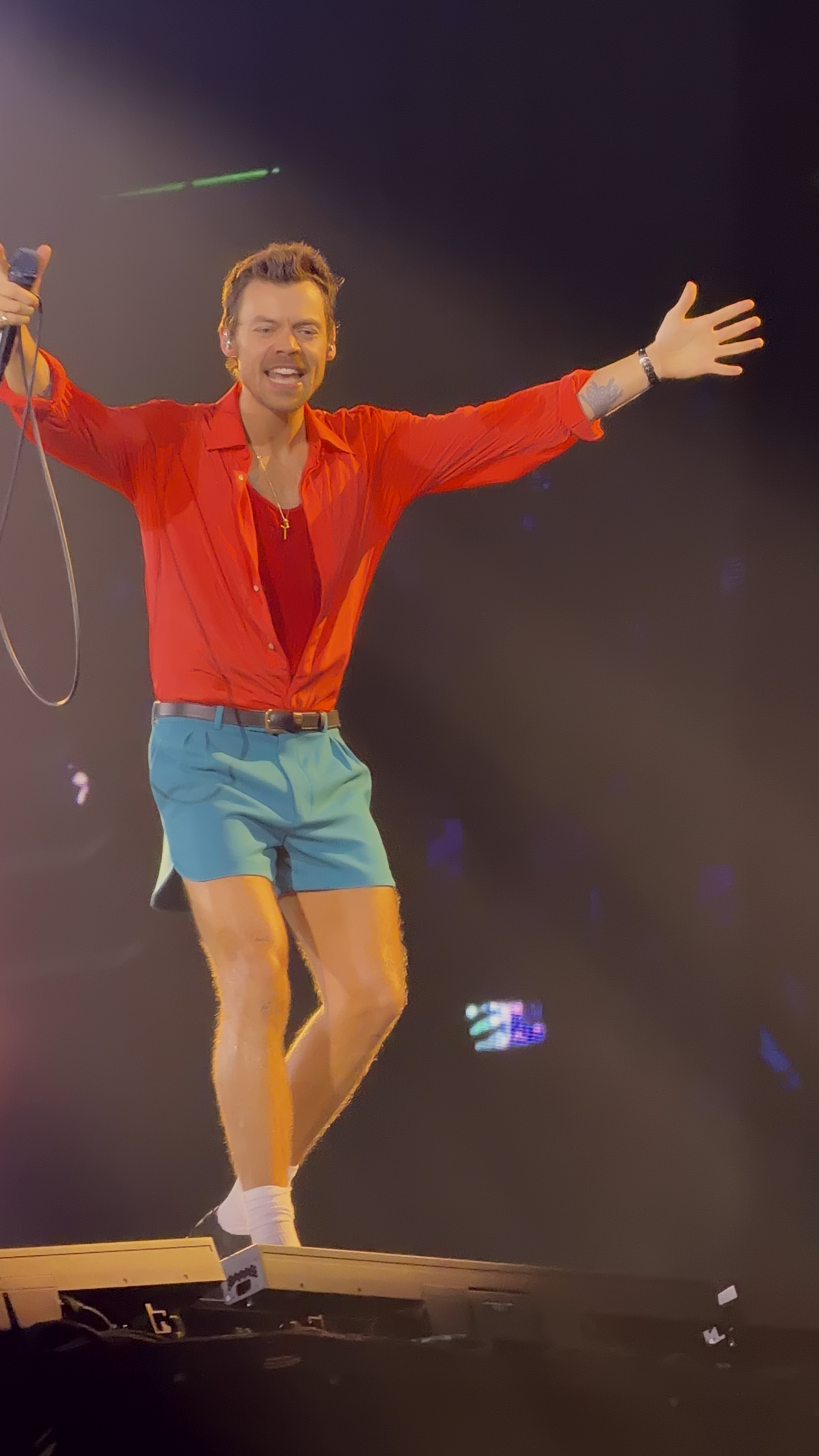 Harry Styles on stage in 2026, red shirt, arms wide
