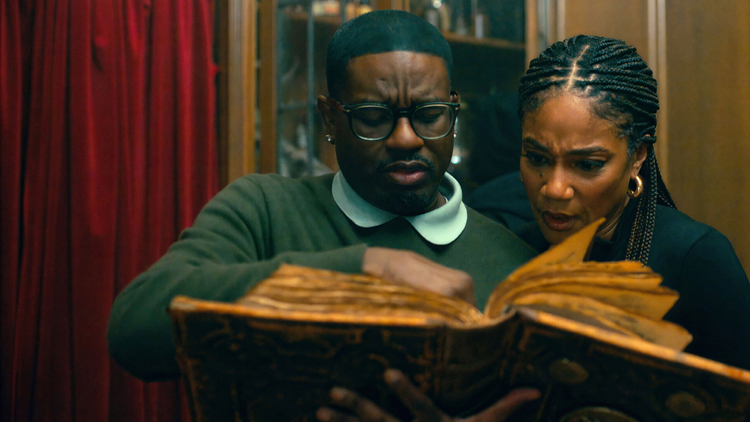 Ron (Lil Rel Howery) and Shari (Tiffany Haddish) pore over an ancient book inside the mansion in Haunted Heist