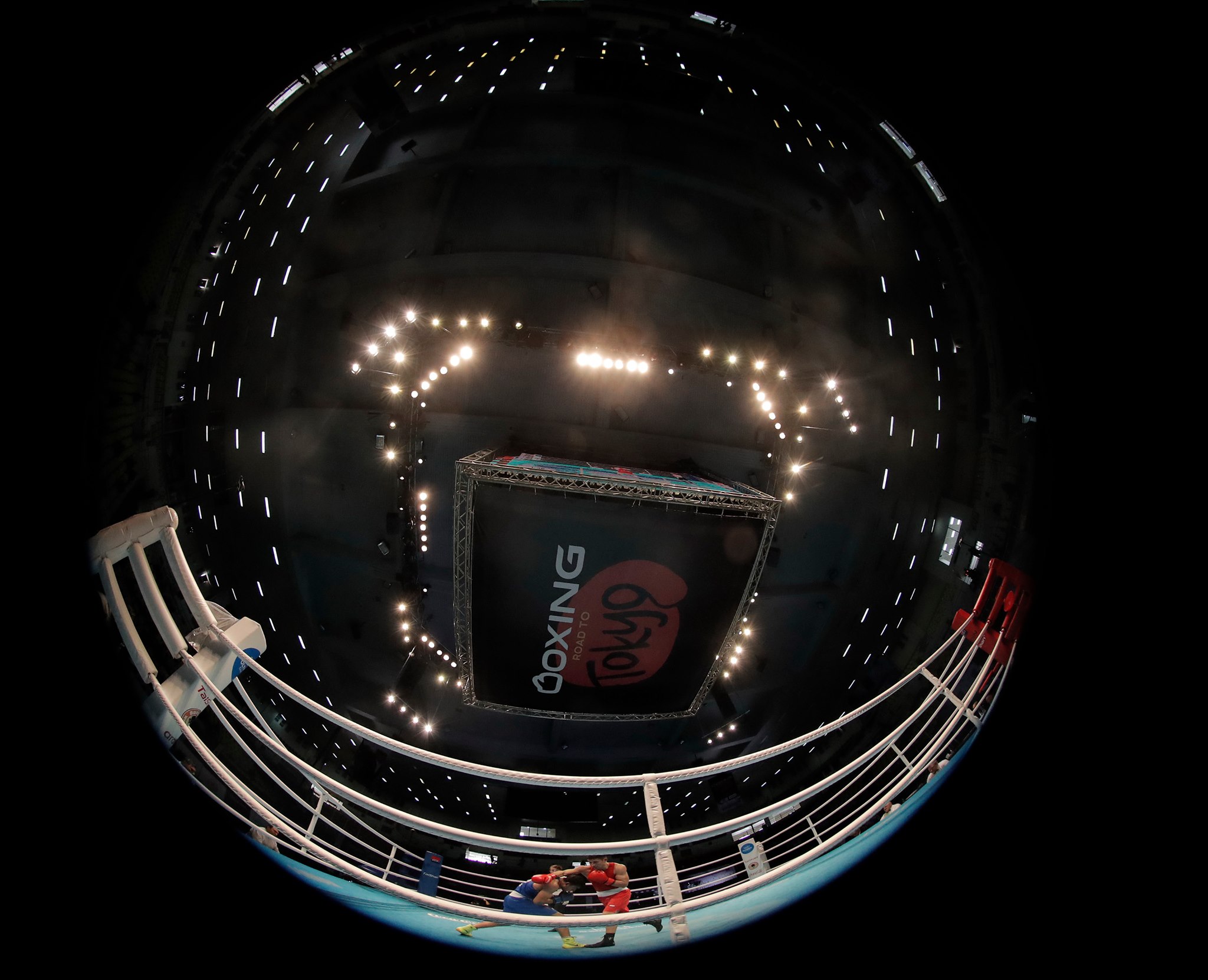 A boxing ring under bright arena lights, viewed through a fisheye lens
