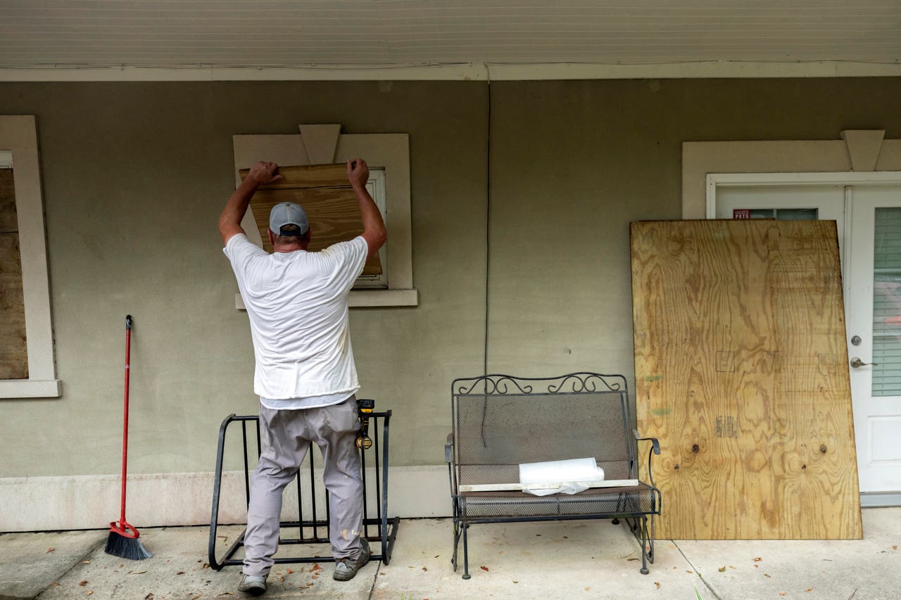 A Florida homeowner boards up windows with plywood ahead of the approaching storm
