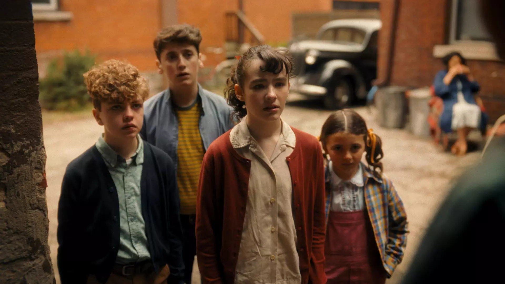The four young leads of It: Welcome to Derry standing in a 1962 Derry alley, a period car behind them