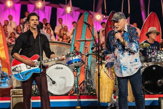John Stamos performing with The Beach Boys at a concert.