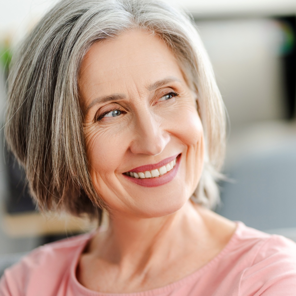 A confident older woman with natural gray hair smiling in soft daylight